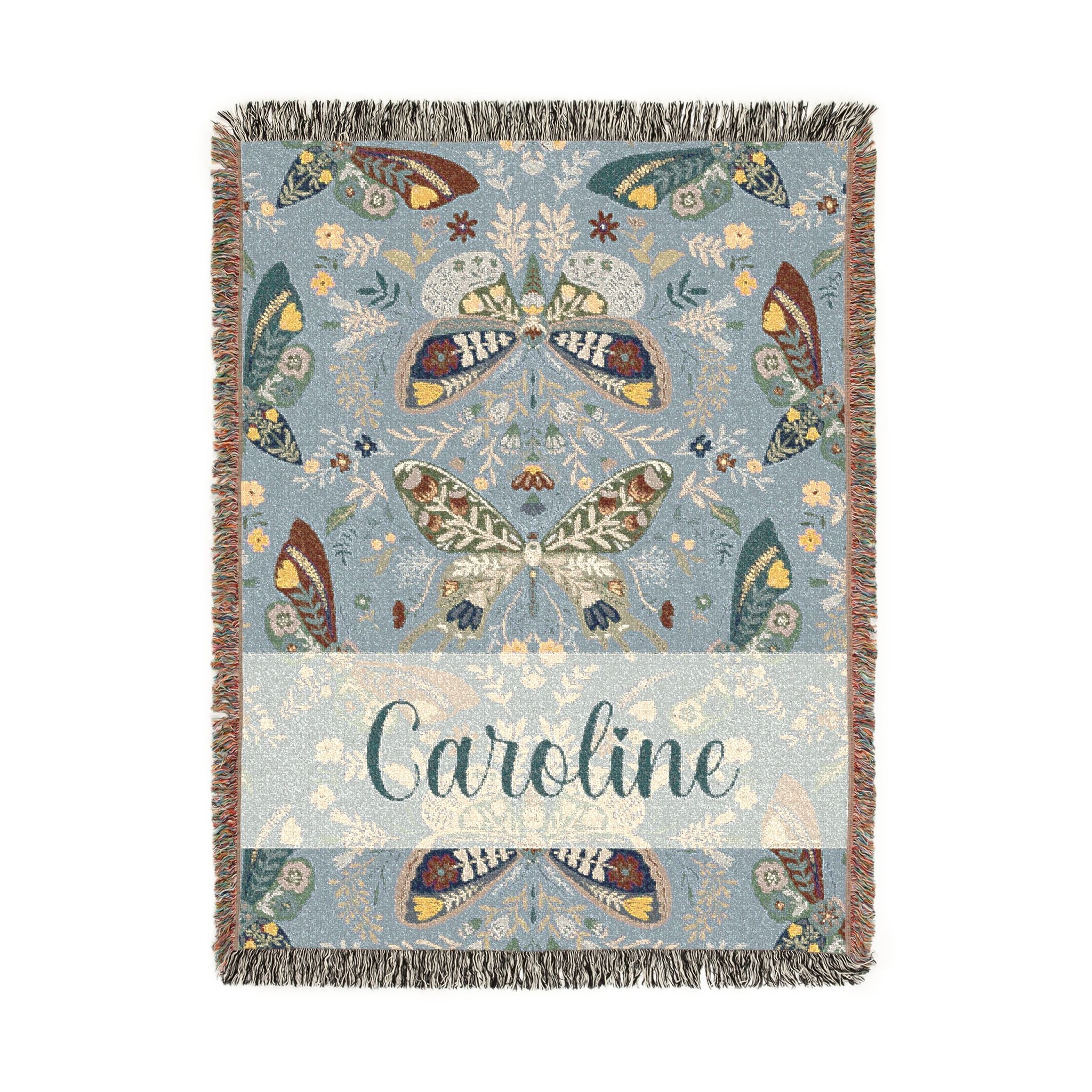 Decorative blanket with butterfly pattern and 'Caroline' text on a light blue background