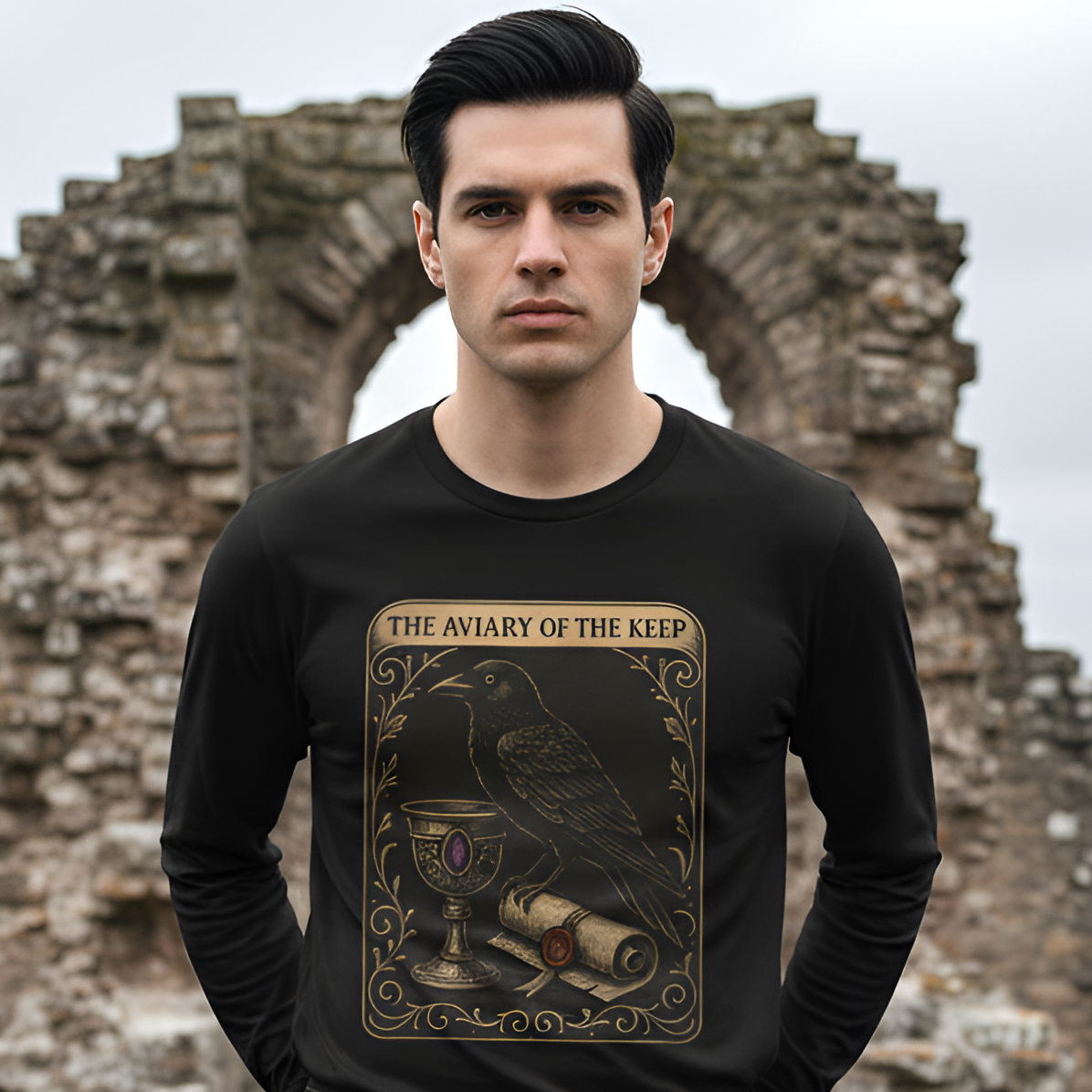 Man wearing a black sweatshirt with 'The Aviary of the Keep' design in front of stone ruins.