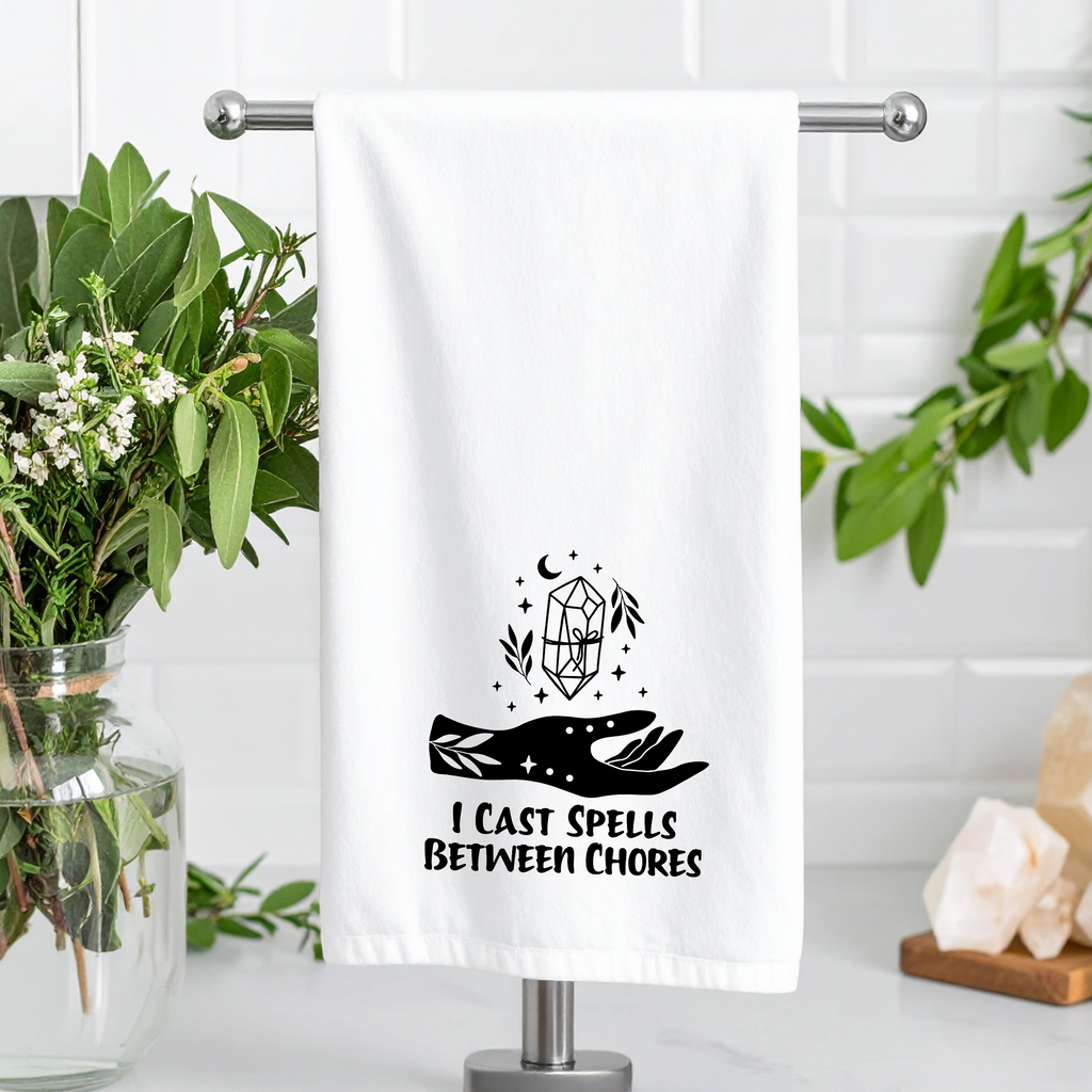 Towel with 'I Cast Spells Between Chores' design on a stand with plants and decor.