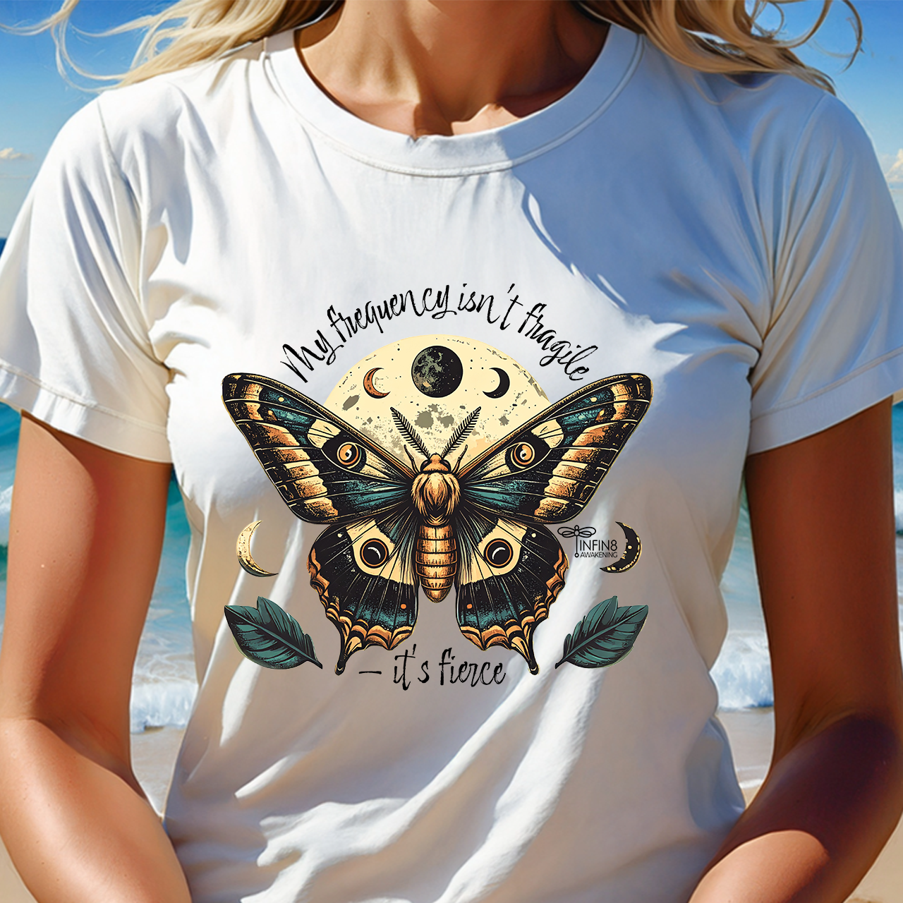 Person wearing a white t-shirt with a butterfly design and text on a beach.