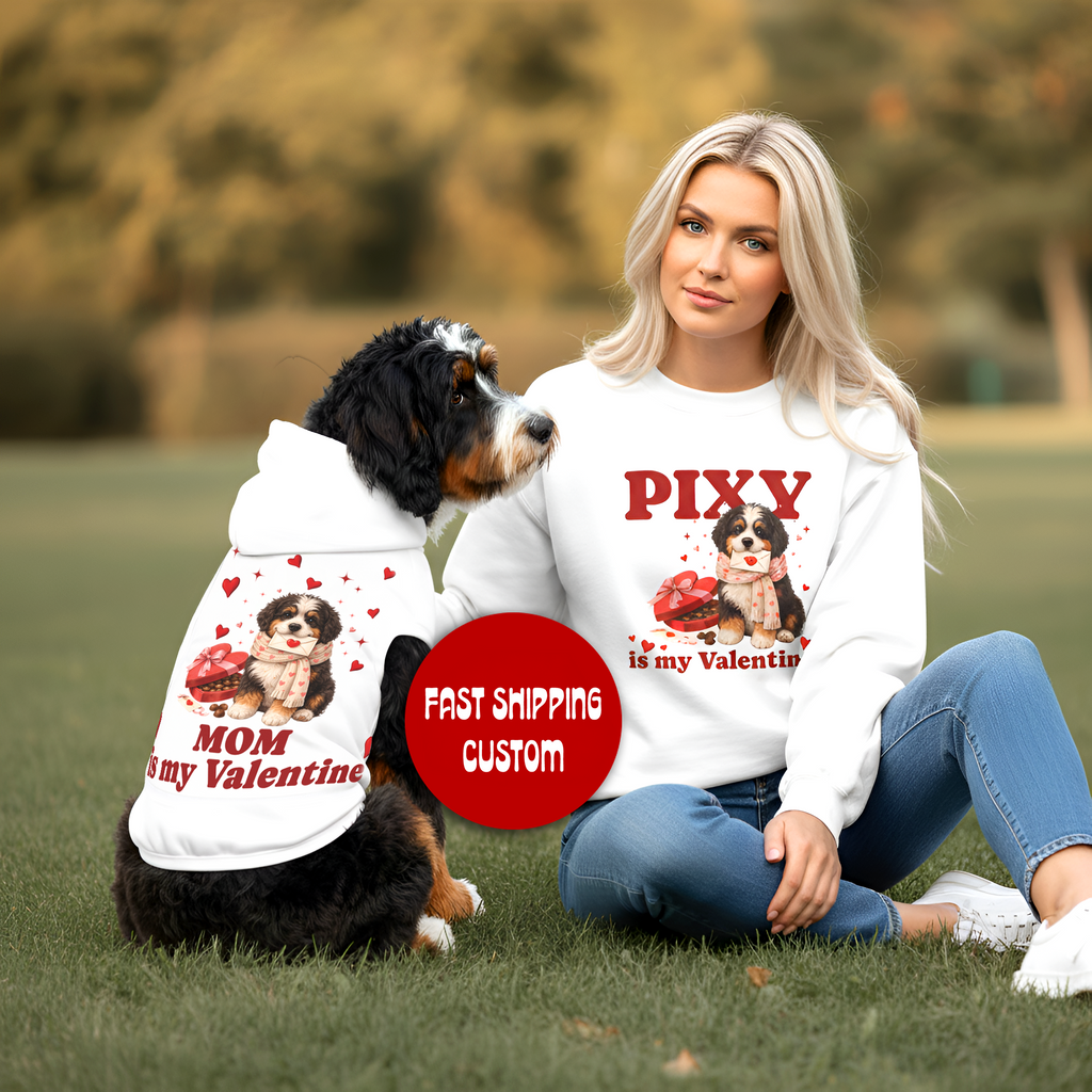 Woman and dog wearing matching Valentine-themed shirts in a park setting.
