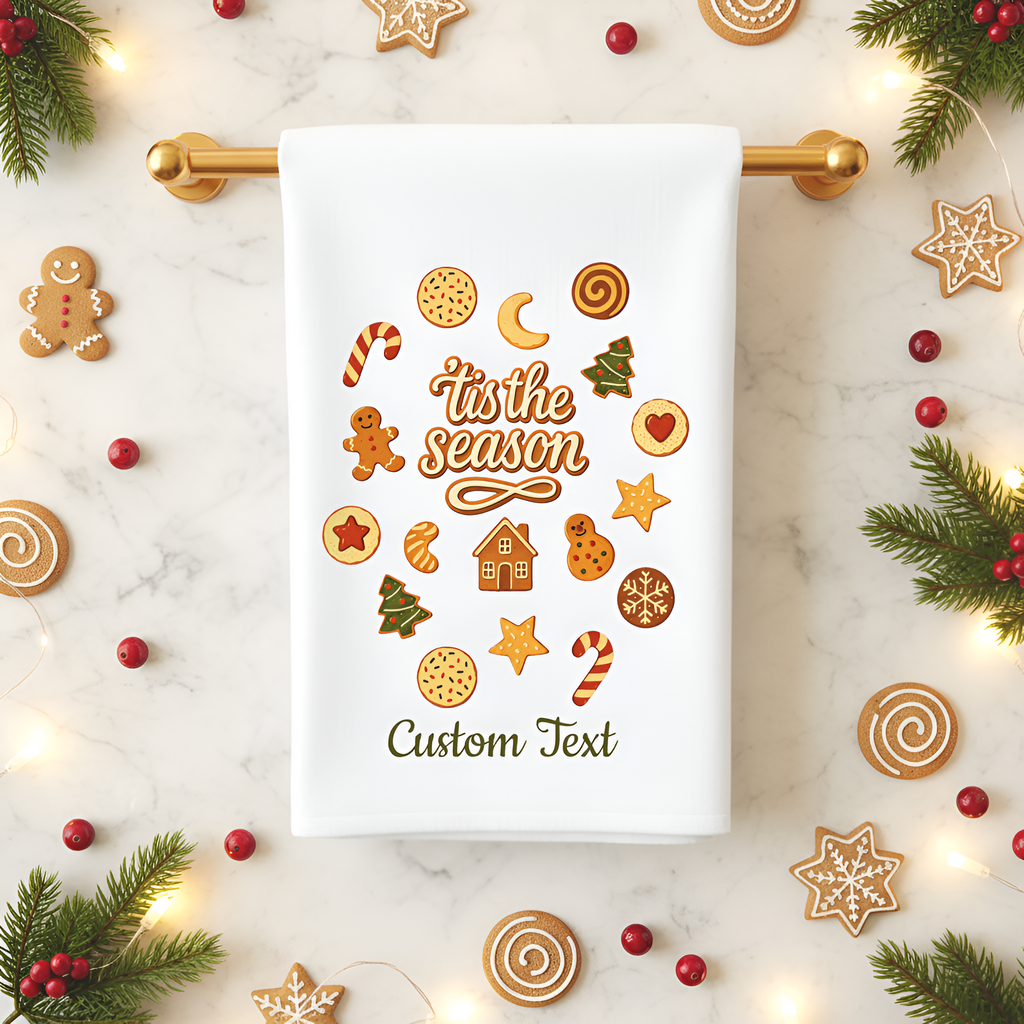 Decorative towel with 'tis the season' text and festive graphics on a marble surface with Christmas decorations.